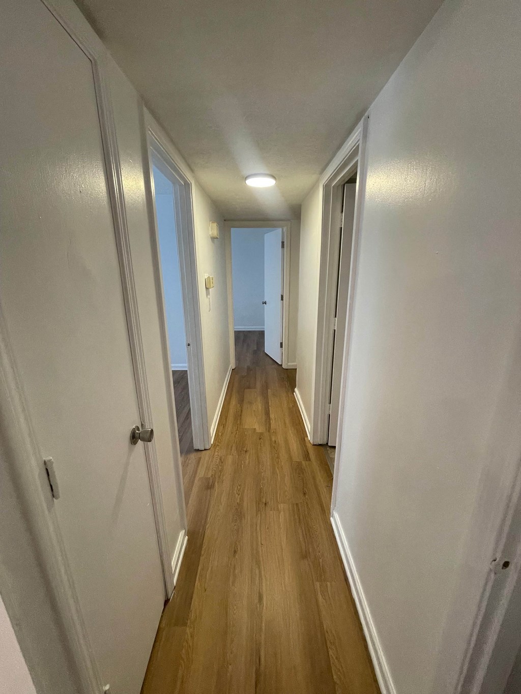 a hallway with wood floors and white walls and a door to a bedroom