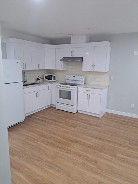 an empty kitchen with white cabinets and appliances and a wooden floor