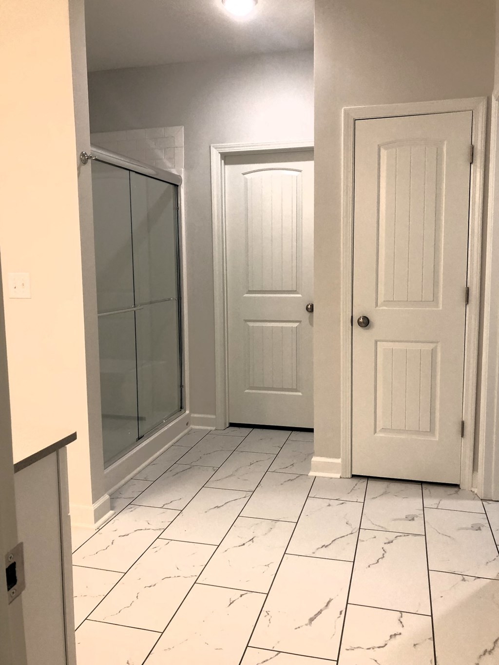 a bathroom with two doors and a tiled floor and a shower