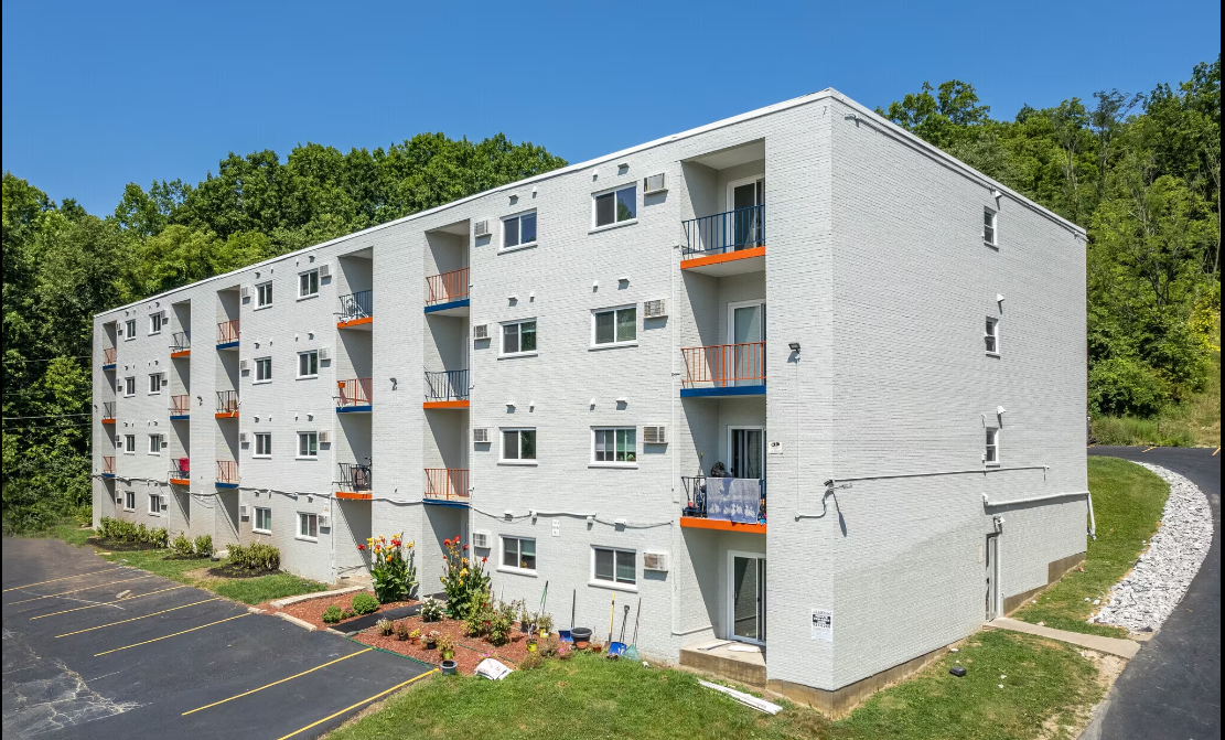 A white apartment building with orange railings and a parking lot in front.