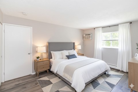A bedroom with a large bed, a nightstand with a lamp, and a window with curtains.