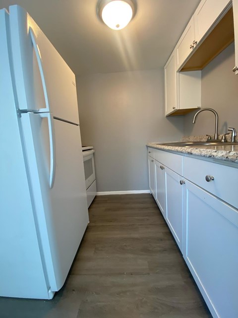 A white refrigerator is in a kitchen with white cabinets.