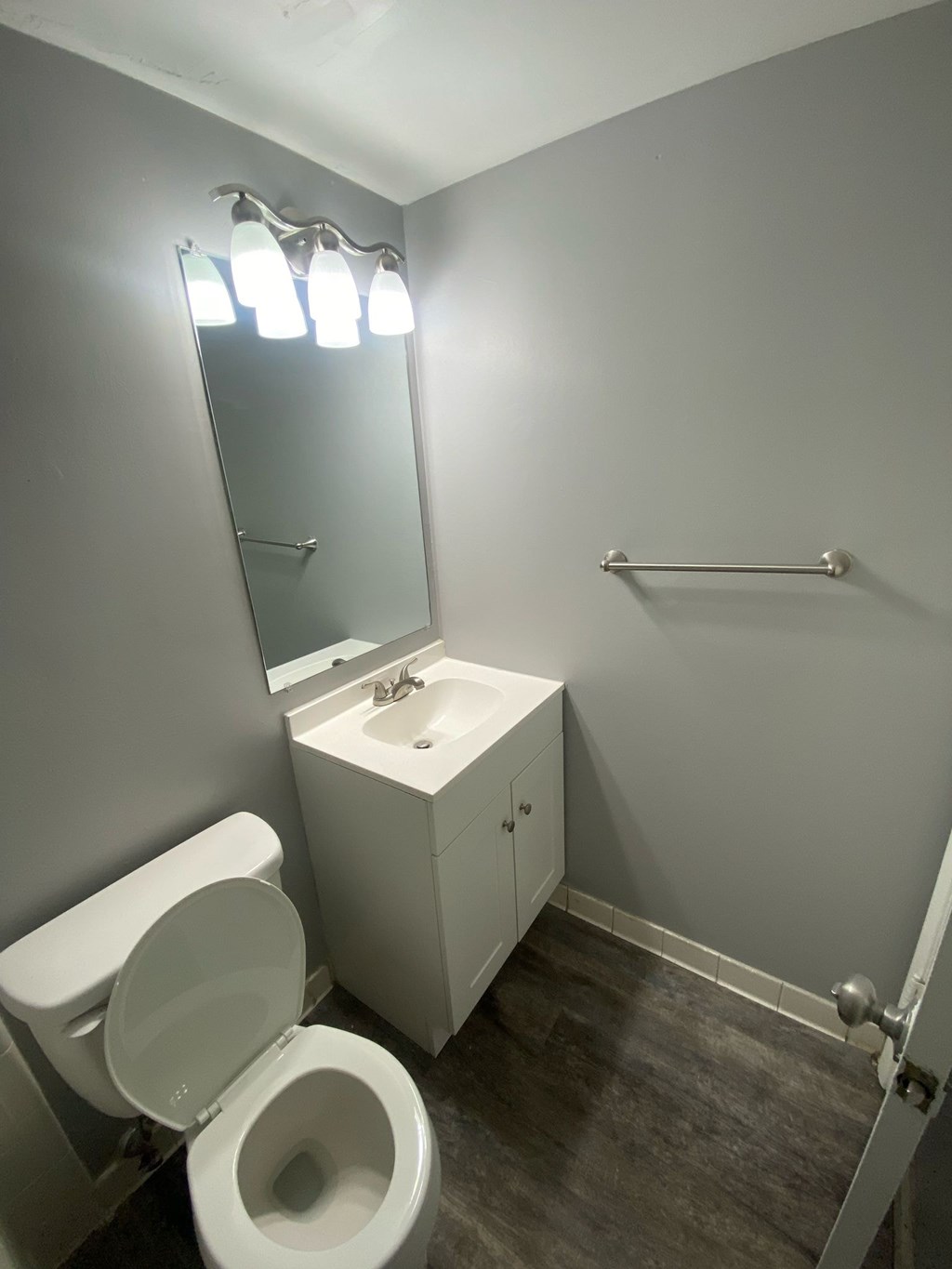 A bathroom with a toilet, sink, mirror, and light fixture.
