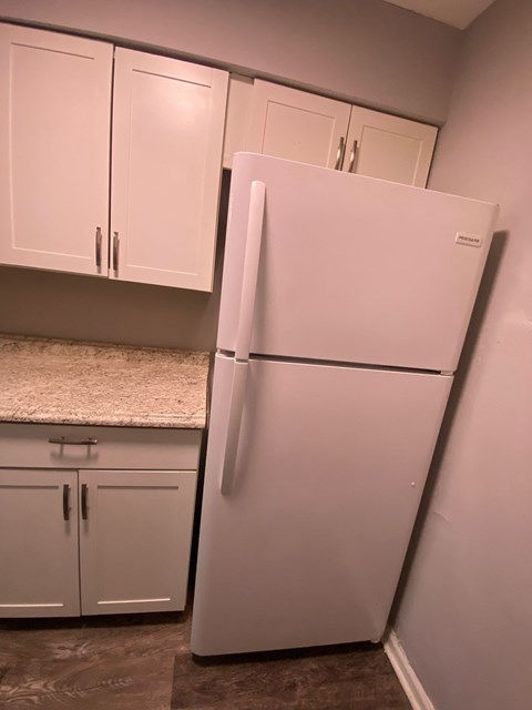 A white refrigerator stands in a kitchen next to white cabinets.