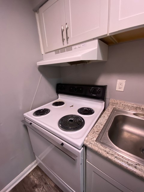 A white stove top oven with four burners and a stainless steel sink in a kitchen.