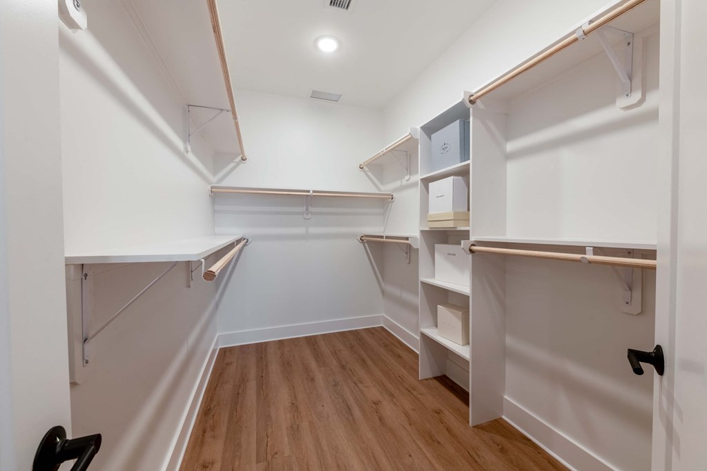 a walk in closet with white walls and wooden floors