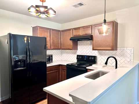 A black refrigerator is in a kitchen with brown cabinets and a black stove.