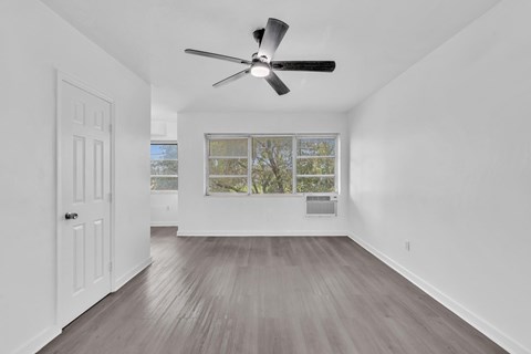 A room with a ceiling fan and a window with a view of trees.