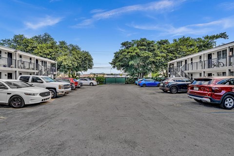 A parking lot with several cars parked in front of apartment buildings.