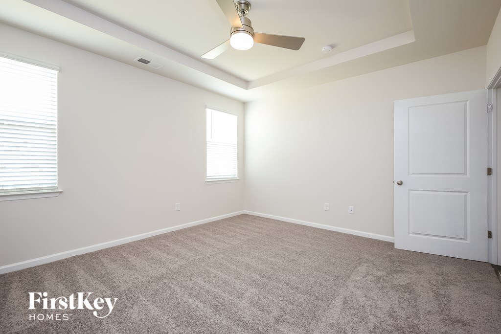 A room with a carpeted floor, a ceiling fan, and a door.
