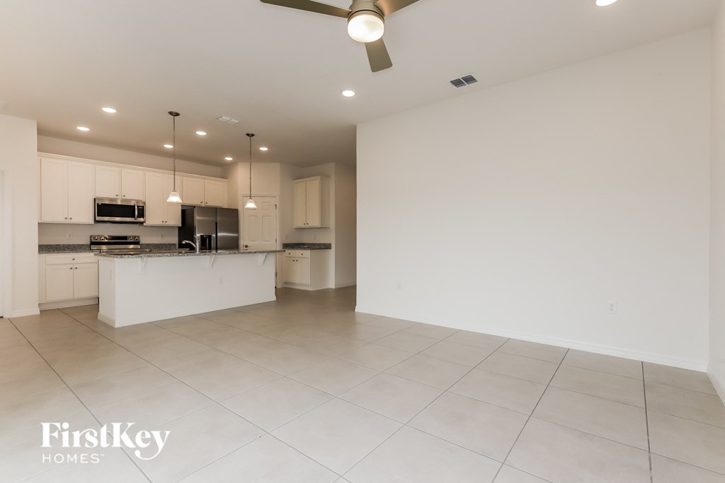 an empty kitchen and living room with white tile floors and white cabinets