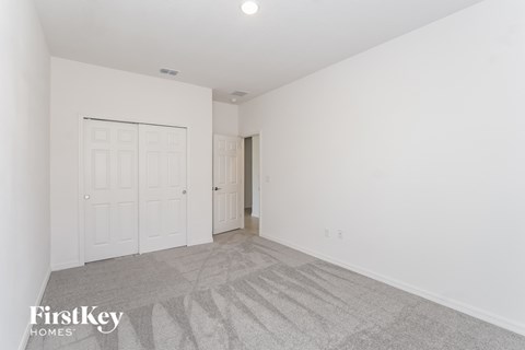 a bedroom with white walls and carpet and a door to a closet