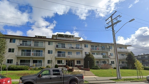 A grey truck is parked in front of a multi-story apartment building.