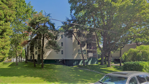 A car is parked in front of a building with a green lawn and trees.