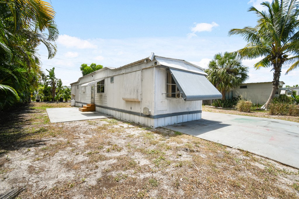 a small white house with a driveway and palm trees