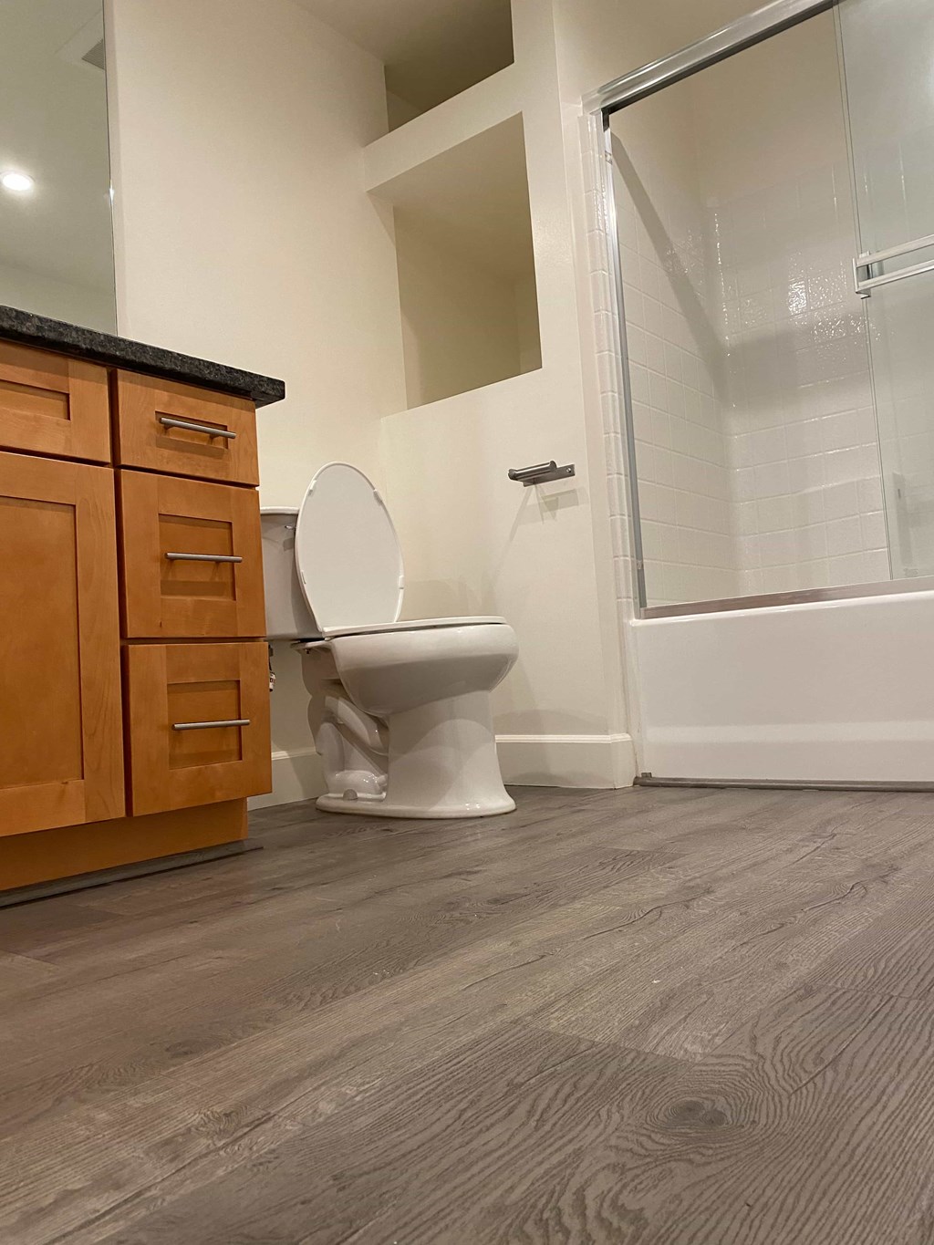 A white toilet sits in a bathroom with wood flooring and a wooden cabinet.