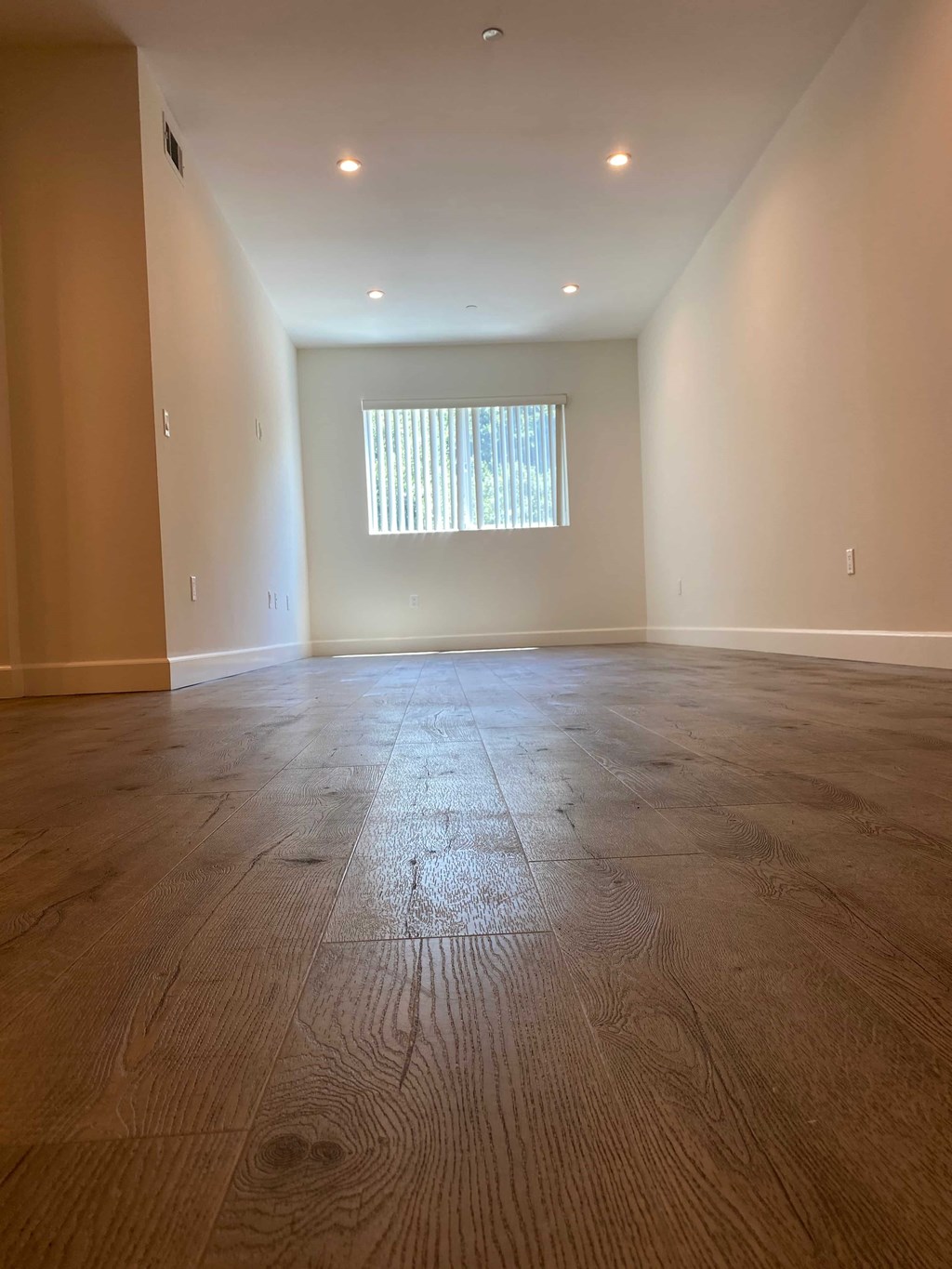 A room with wooden flooring and a window with blinds.