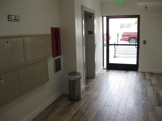 A hallway with a trash can and a door leading to a parking lot.