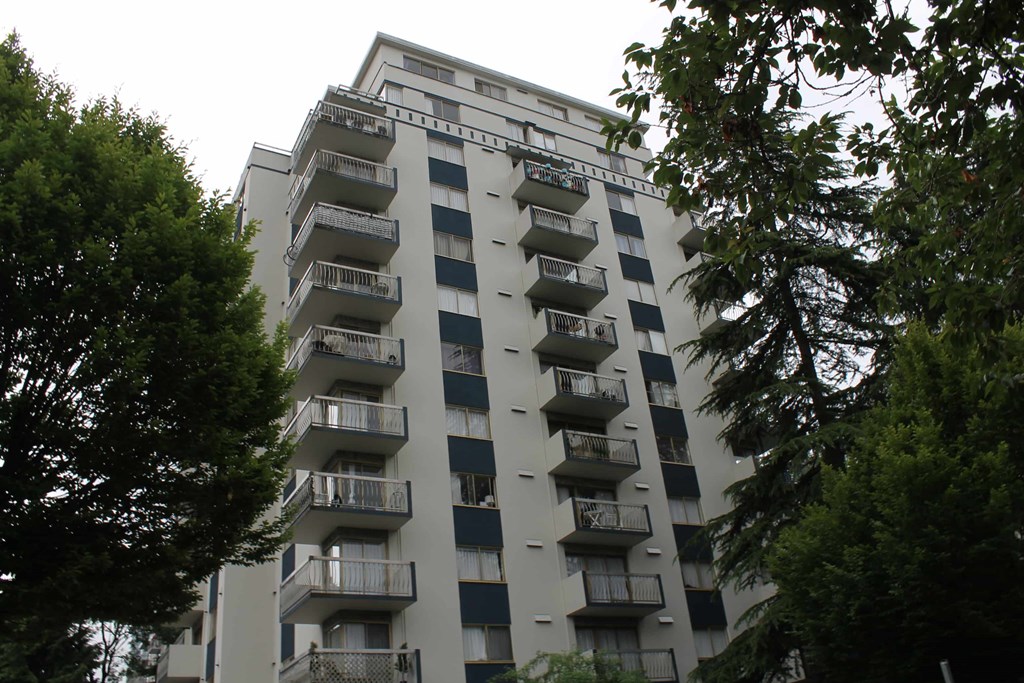 A tall apartment building with balconies and trees in the foreground.