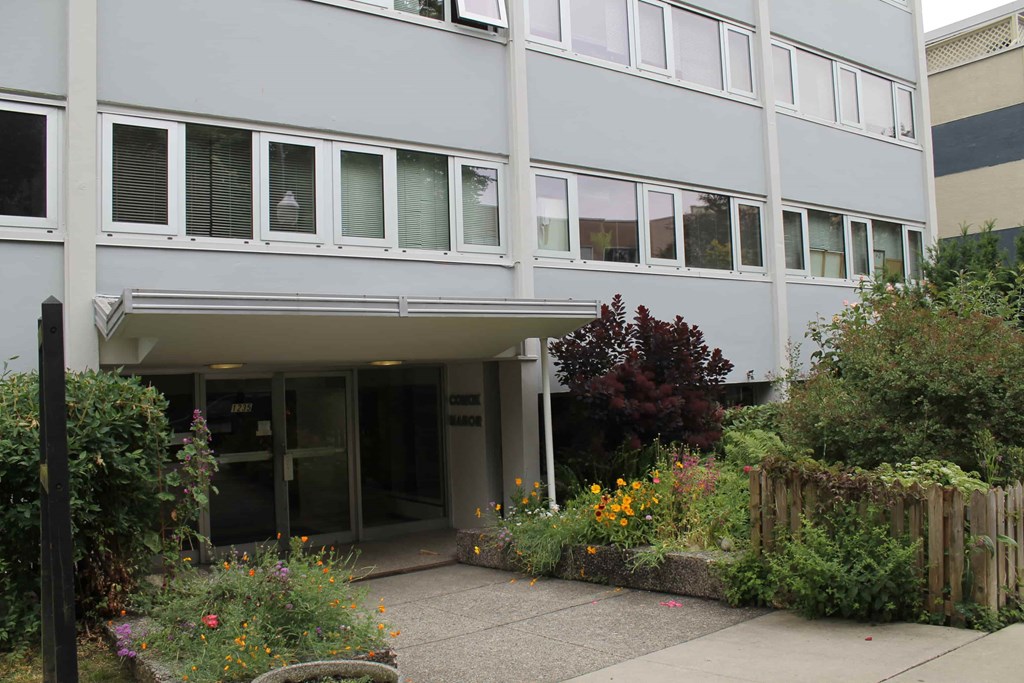 A grey building with a small garden in front.