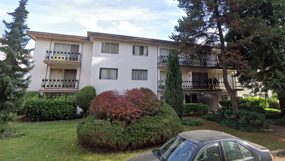 A car is parked in front of a white building with balconies.