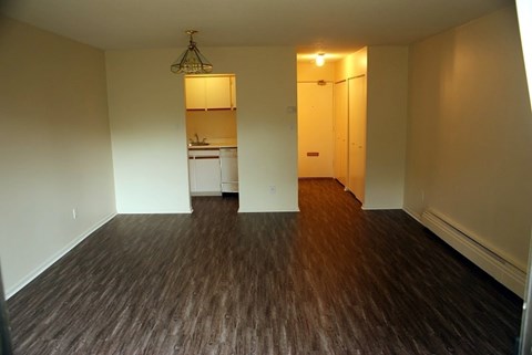 A room with wooden floors and a kitchen in the background.