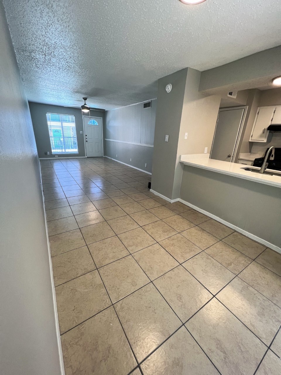 an empty room with a tiled floor and a kitchen in the background