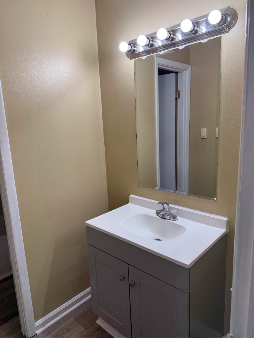 A bathroom with a sink and a mirror with lights on it.