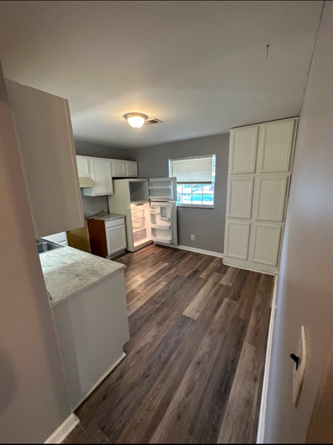 A kitchen area with a refrigerator, cabinets, and a window.