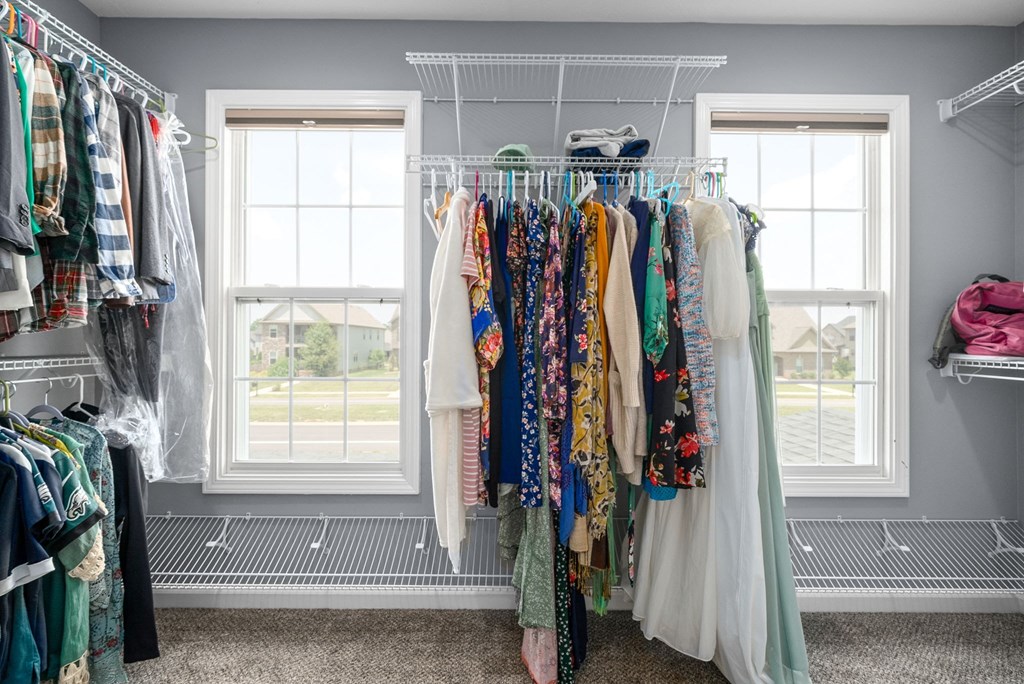 a rack of clothes in a closet with two windows