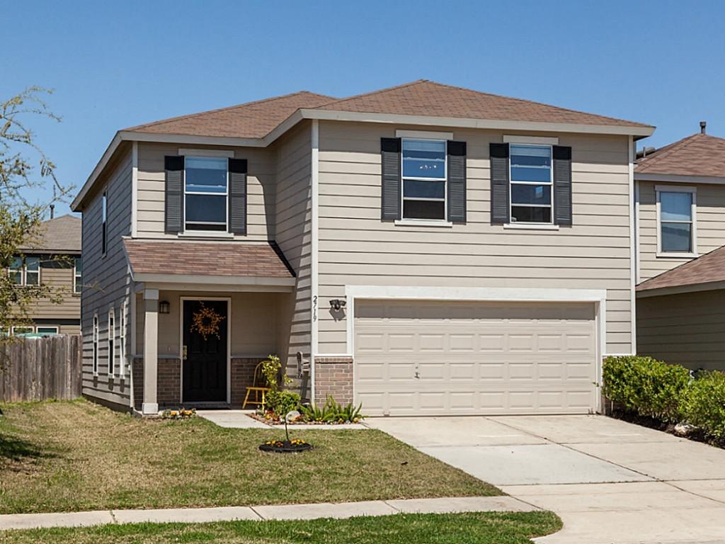 a tan house with a garage door and a lawn