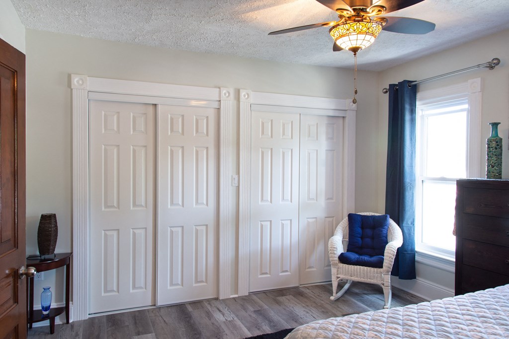 a bedroom with three closet doors and a chair and a ceiling fan