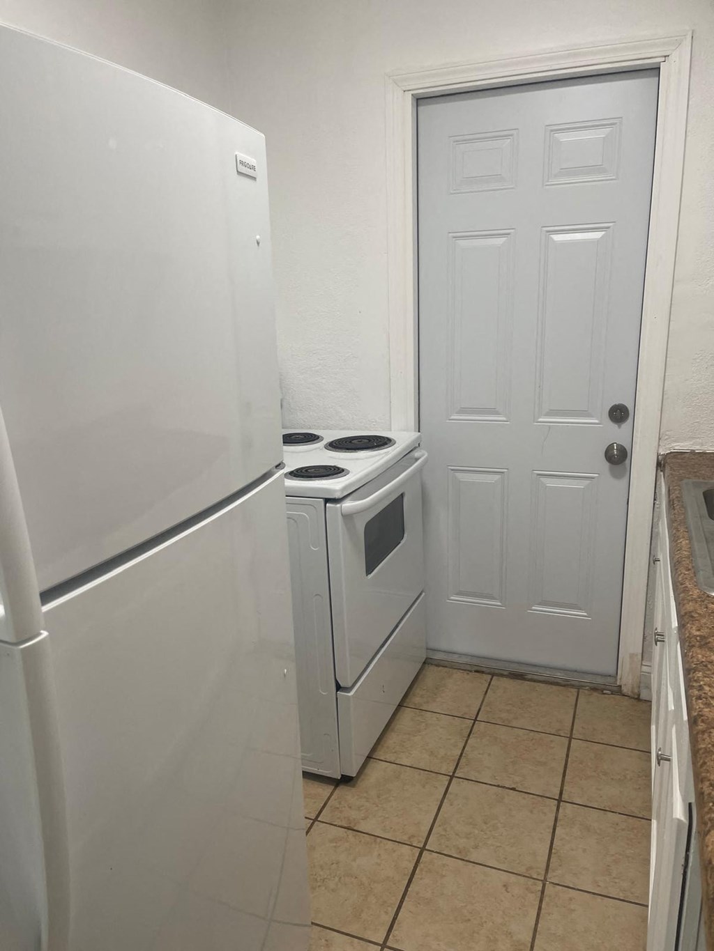 A white refrigerator is in a kitchen next to a white door.