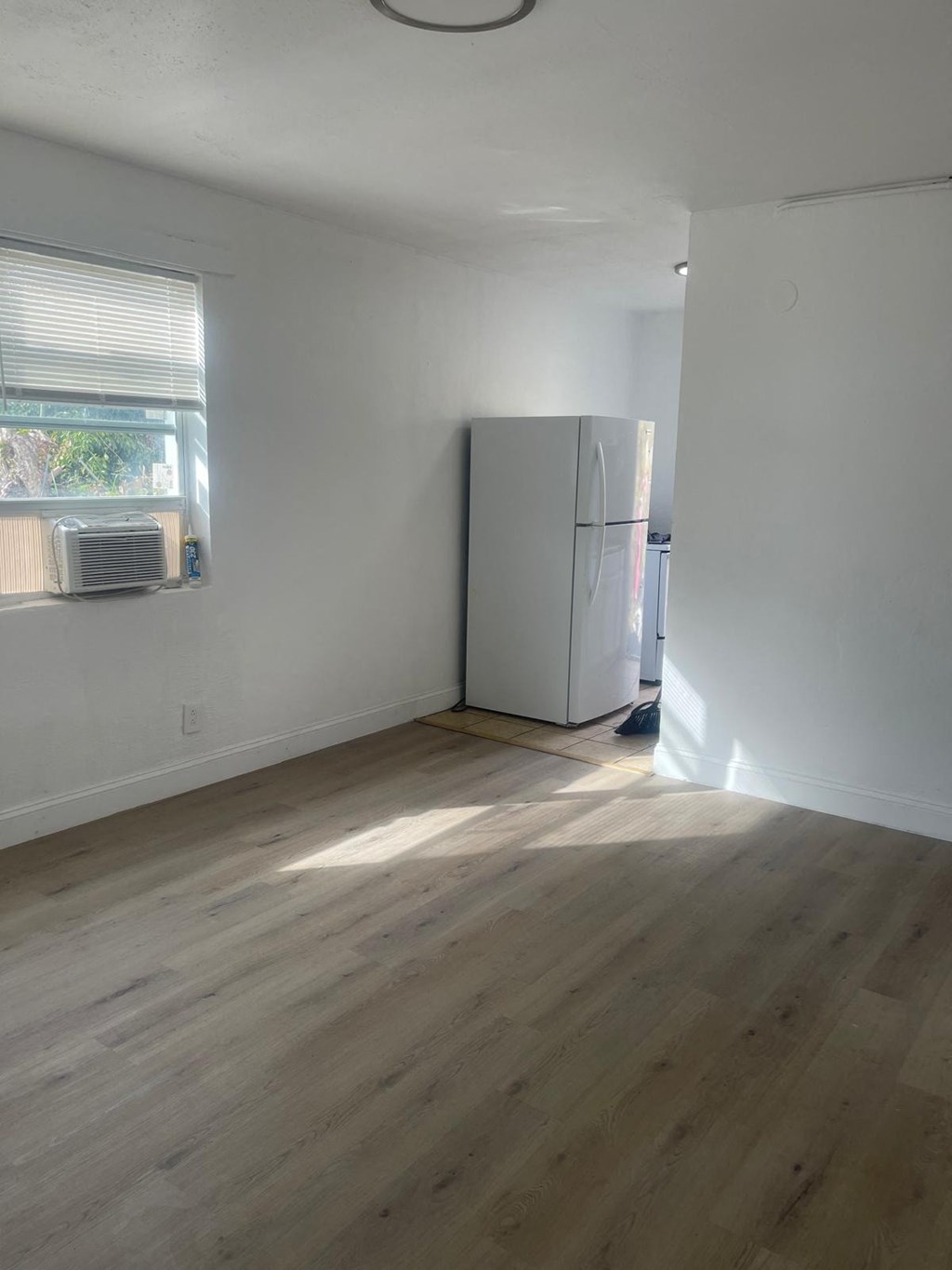 A room with a white wall and a white fridge.