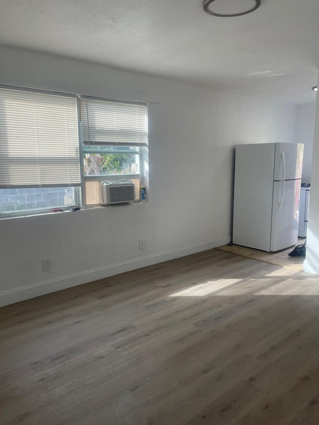 A room with a white refrigerator and wooden flooring.