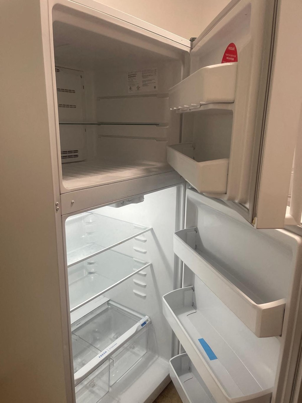 A white refrigerator with the door open showing the empty shelves.