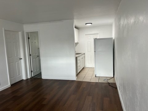 A kitchen with white cabinets and a white refrigerator in a room with wooden floors.