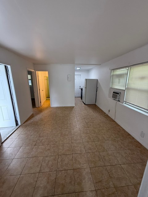 A spacious room with tile flooring and a refrigerator in the corner.