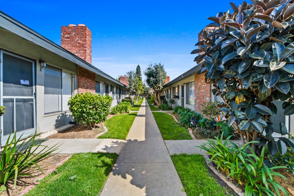 a sidewalk in front of a building with plants and trees