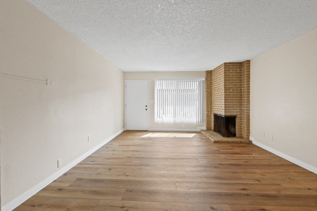 an empty living room with a brick fireplace and wooden floors