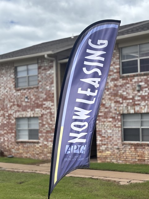 A purple banner with the words "Now Leasing" is displayed in front of a brick building.