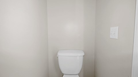 an empty bathroom with a toilet and a white wall
