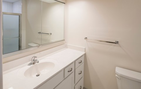 A white bathroom with a sink, mirror, and toilet.
