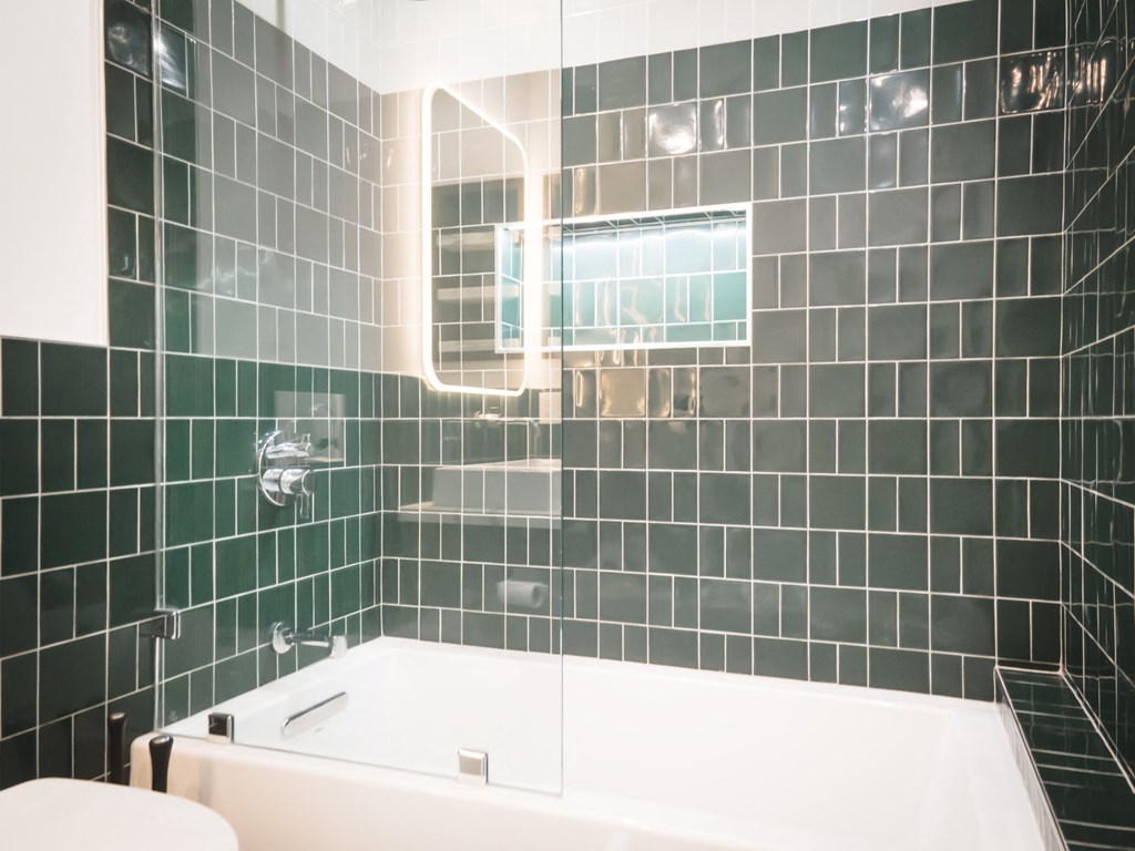 a green tiled bathroom with a tub and a toilet