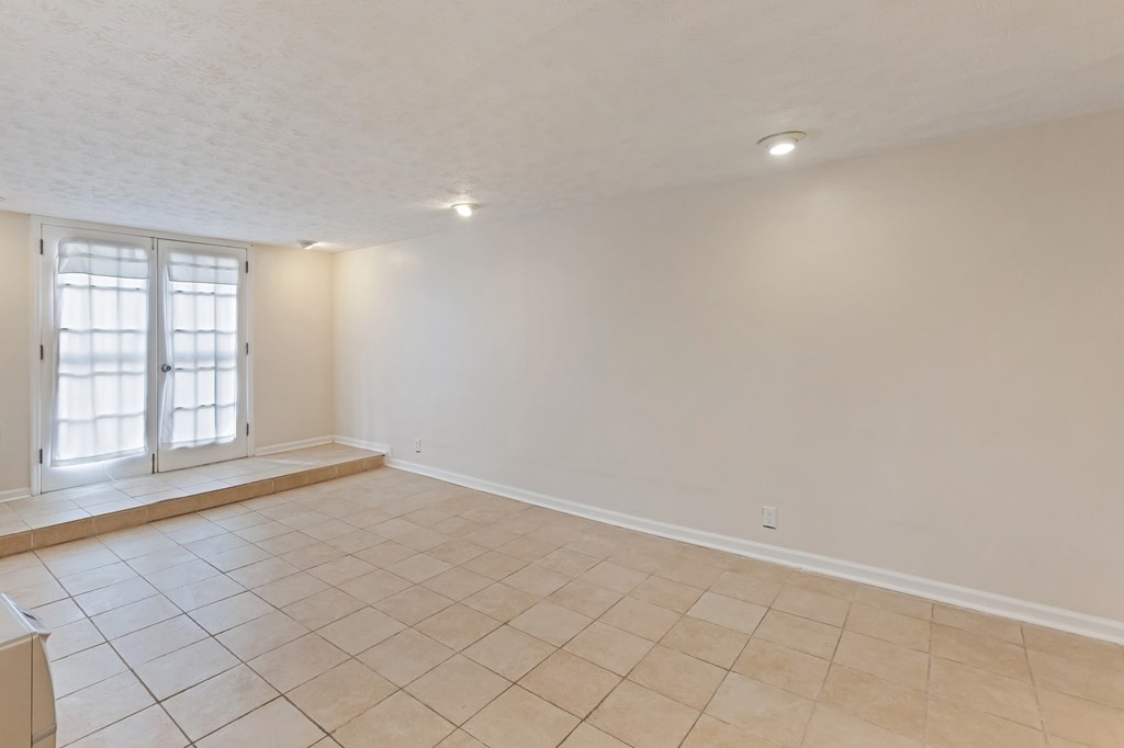 A spacious room with tiled flooring and a window with blinds.