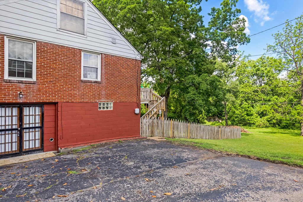 A red brick house with a wooden fence and green trees in the background.