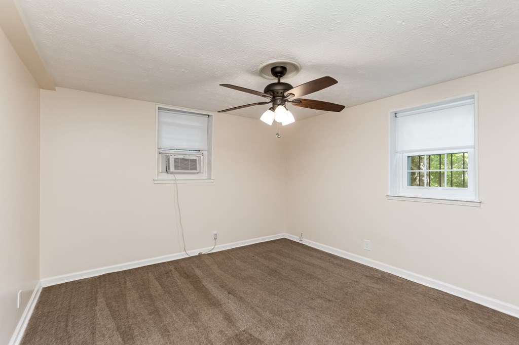 A room with a ceiling fan and two windows.