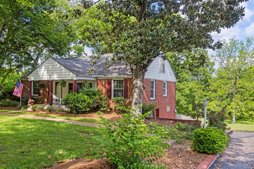 A house with a flag on the porch is surrounded by greenery.