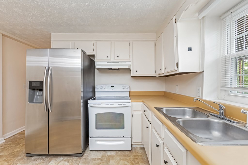 A kitchen with a stainless steel refrigerator, white oven, and white cabinets.