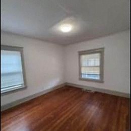 an empty room with a hard wood floor and two windows